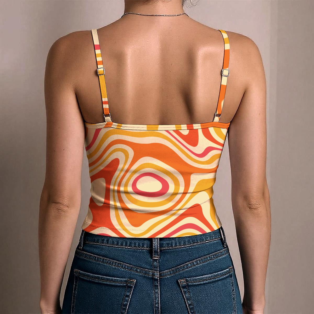 A woman shown from the back wearing a retro-style spaghetti-strap top with a bold wavy abstract pattern in orange, yellow, cream, and pink, paired with blue jeans.
