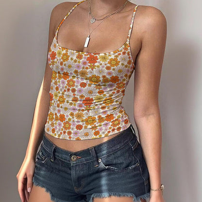 A woman wearing a fitted spaghetti-strap camisole top with a retro 70s floral print in orange, yellow, and pink on a white background, paired with dark blue denim shorts.