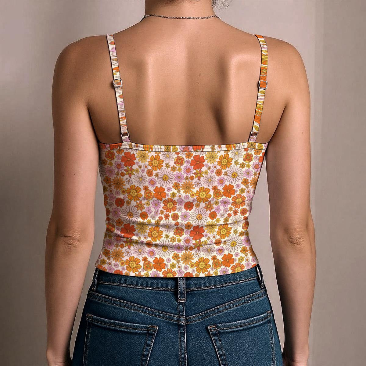 Rear view of a woman wearing a fitted spaghetti-strap tank top with a retro orange, yellow, and pink floral pattern, paired with blue jeans against a neutral beige background.